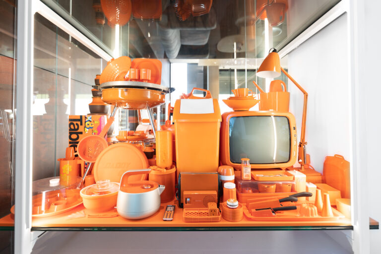 An assortment of orange-coloured design objects on display in a glass showcase