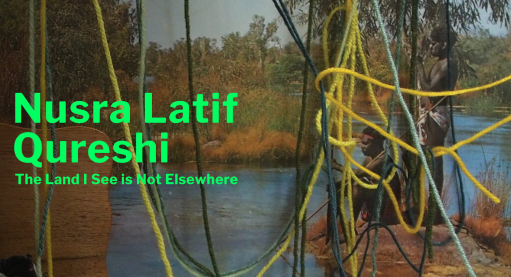 A photo of an art installation featuring an archival photo of two Aboriginal boys on the bank of a river; the photo is partly obscured by threads of tangled yellow wool. Text to the left reads 'Nusra Latif Qureshi, The Land I See Is Not Elsewhere'