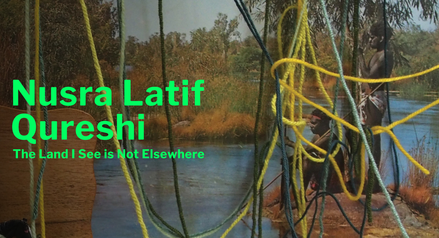 A photo of an art installation featuring an archival photo of two Aboriginal boys on the bank of a river; the photo is partly obscured by threads of tangled yellow wool. Text to the left reads 'Nusra Latif Qureshi, The Land I See Is Not Elsewhere'