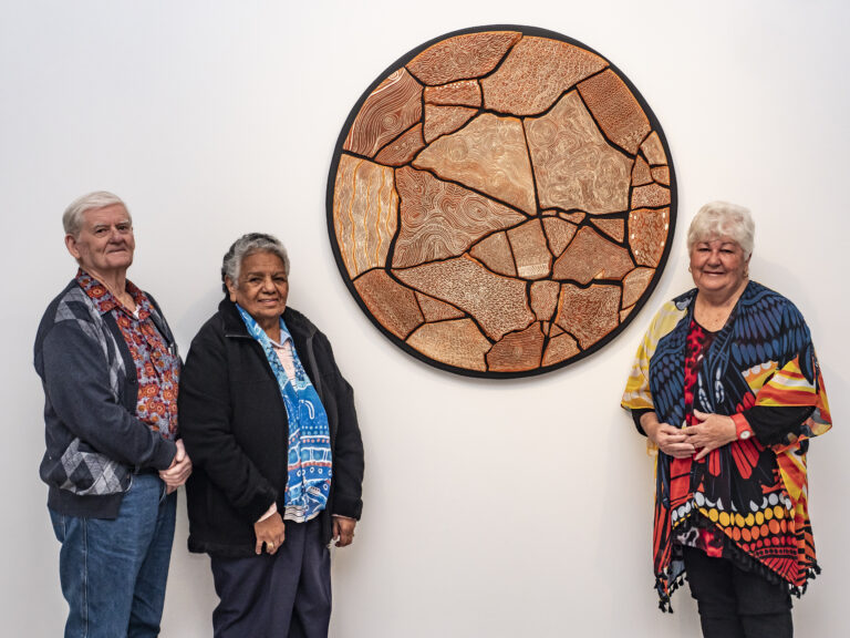 A man and two woman stand to the left and right of their award-winning artwork, a large round terracotta ceramic work mounted on a white wall